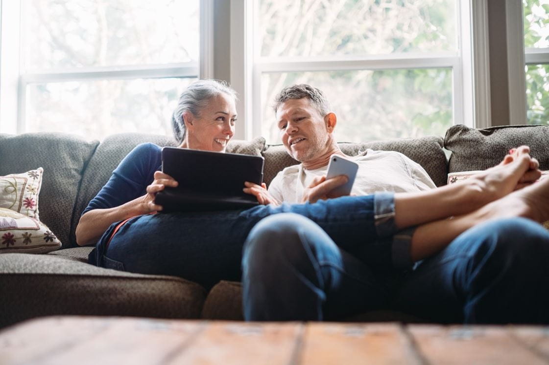 Older man and woman sitting on couch, looking at laptop