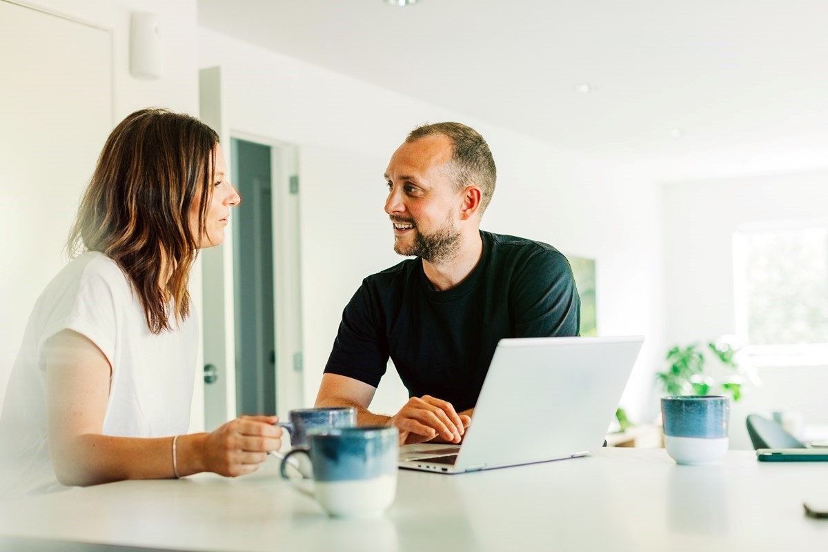 Woman and man smiling and looking at laptop on kitchen bench