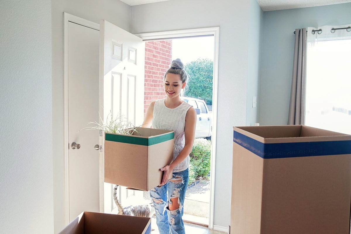Smiling woman carrying a box into her new home