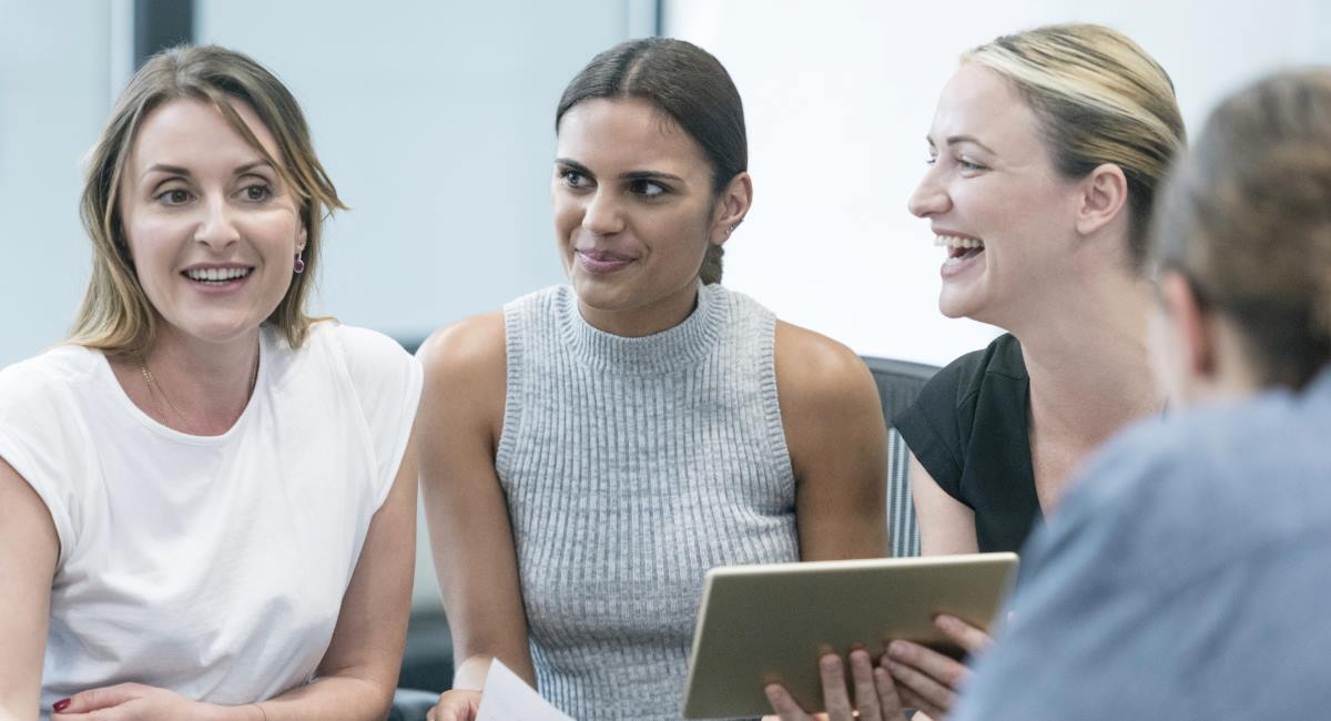 Three women smiling while looking at a notebook