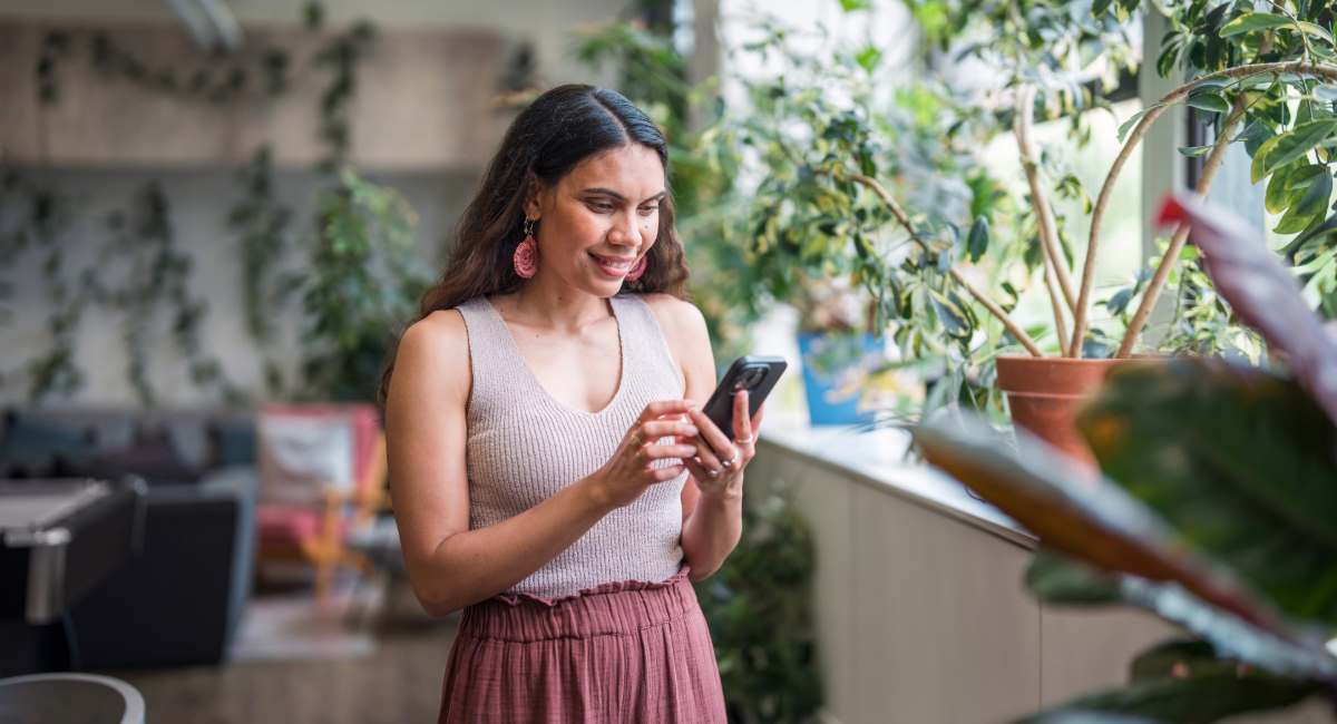An Indigenous woman smiling at her phone in a leafy office