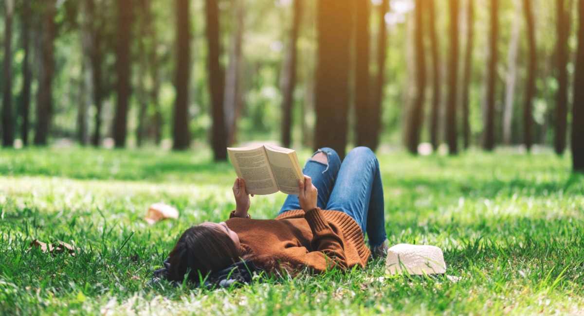 A woman lying in the grass reading a book