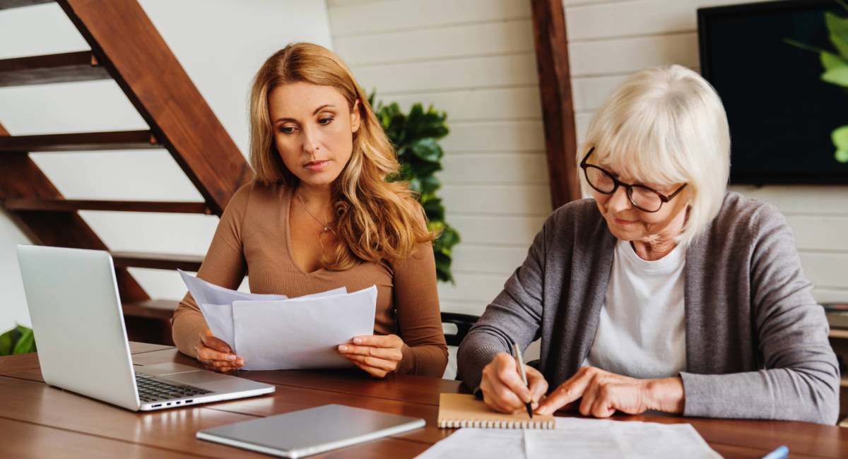 A middle aged woman and an elderly woman looking at paperwork at a desk
