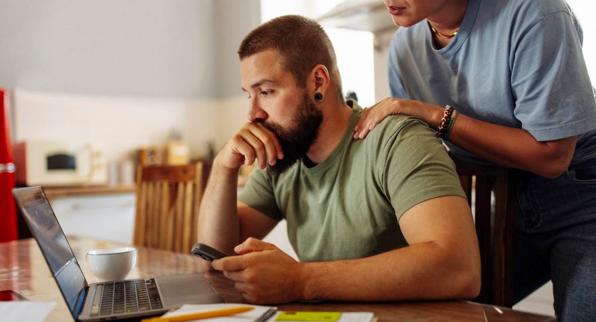A man looking stressed at his computer while a woman comforts him