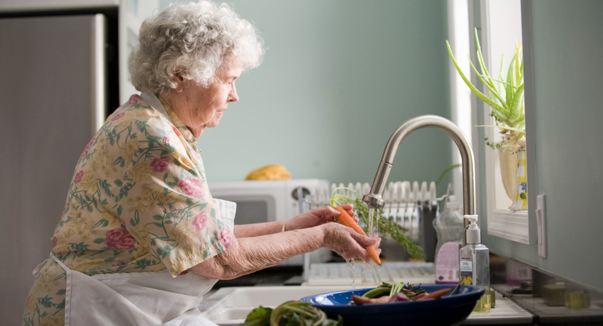 Older woman washing vegetables at sink