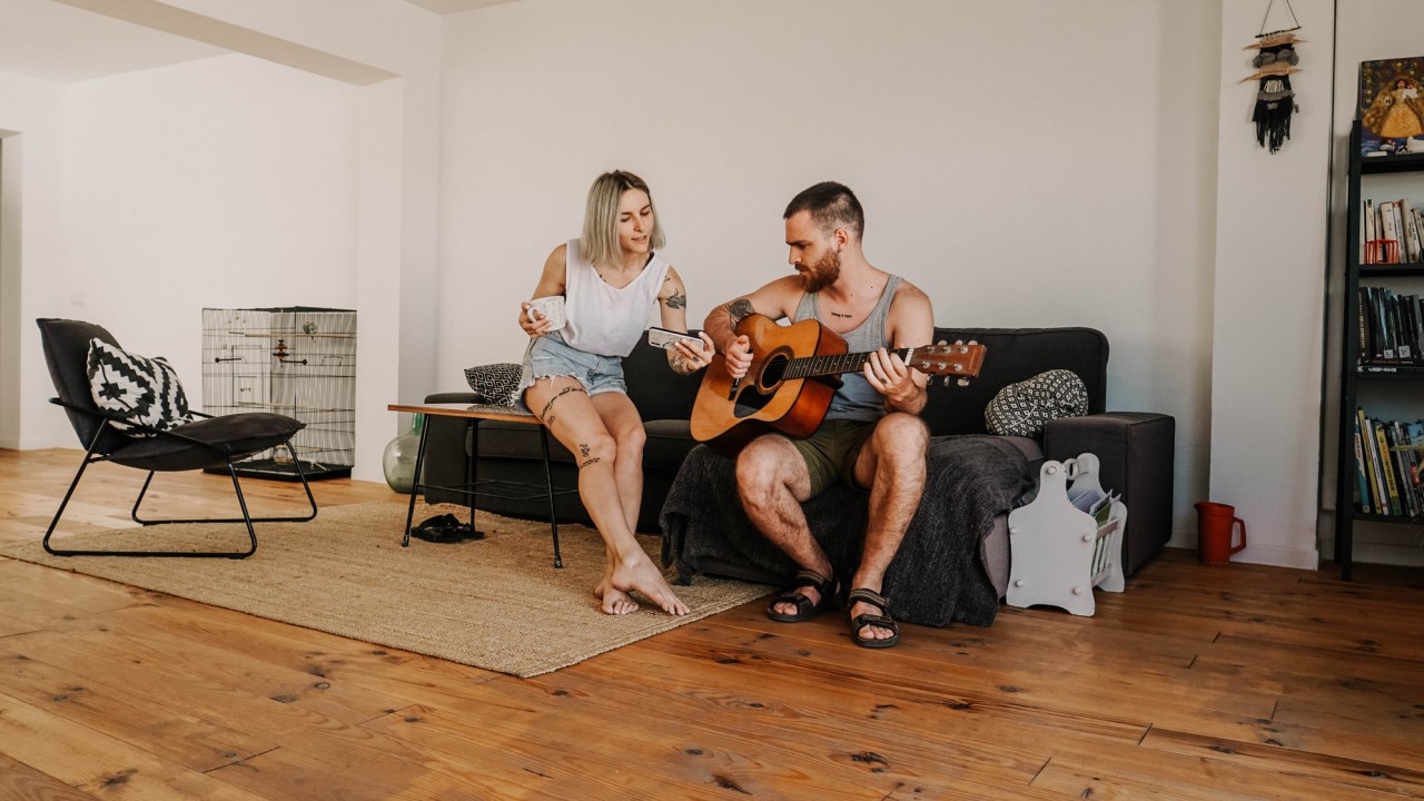 Man strumming a guitar on couch with woman beside him listening