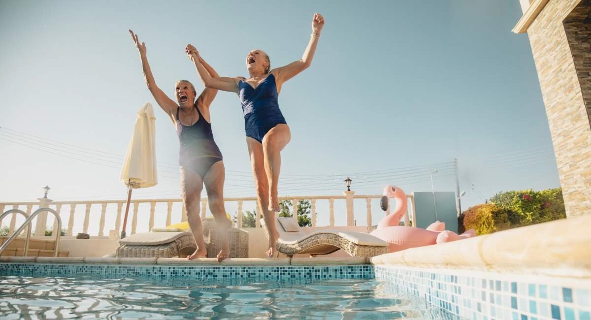 Two middle aged women holding hands while laughing and jumping into a pool