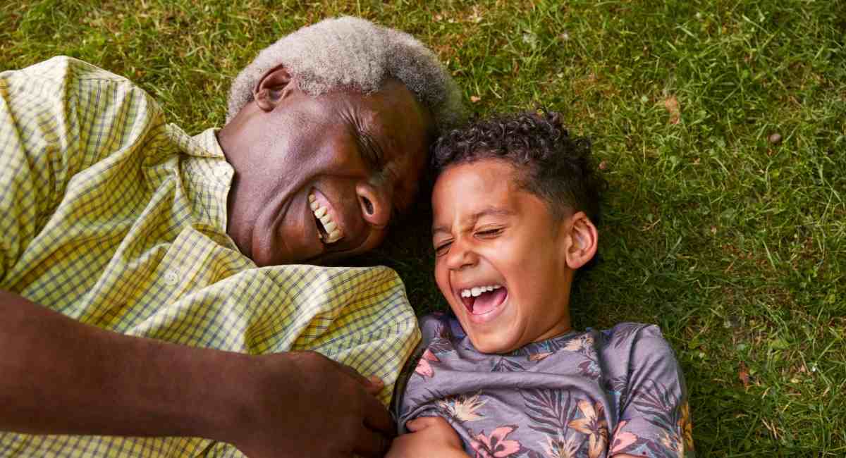 A mature man and young boy lying in the grass laughing