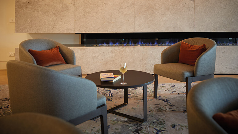 Beige armchairs surrounding a coffee table with fireplace in the background